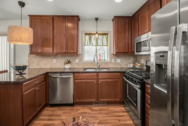 kitchen with decorative light fixtures, tasteful backsplash, appliances with stainless steel finishes, dark stone countertops, and sink