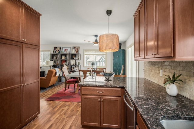 kitchen featuring dark stone countertops, light hardwood / wood-style floors, decorative light fixtures, stainless steel dishwasher, and backsplash