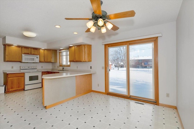 kitchen featuring white appliances, kitchen peninsula, ceiling fan, and a healthy amount of sunlight