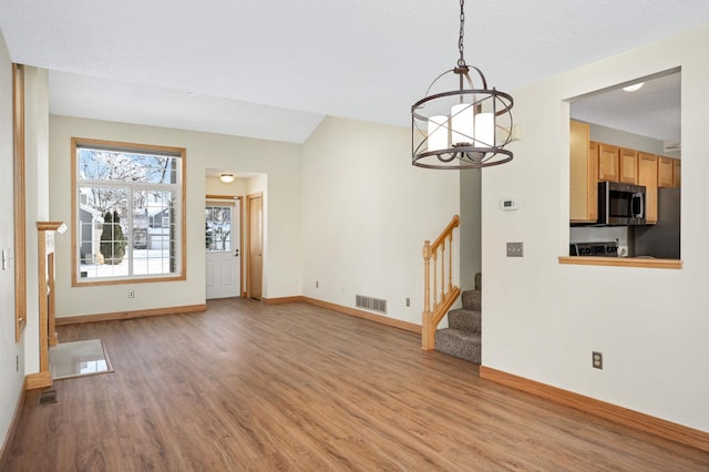 unfurnished living room featuring a notable chandelier, light wood-type flooring, and a textured ceiling