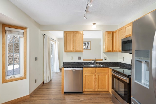 kitchen featuring a textured ceiling, light hardwood / wood-style floors, dark stone counters, appliances with stainless steel finishes, and sink