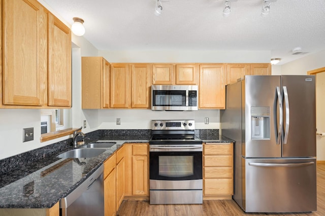 kitchen with appliances with stainless steel finishes, light wood-type flooring, dark stone counters, a textured ceiling, and sink