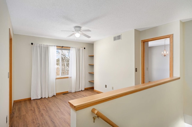 stairway with ceiling fan with notable chandelier, wood-type flooring, and a textured ceiling