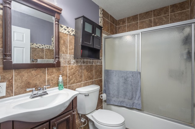 full bathroom with a textured ceiling, vanity, tile walls, toilet, and combined bath / shower with glass door