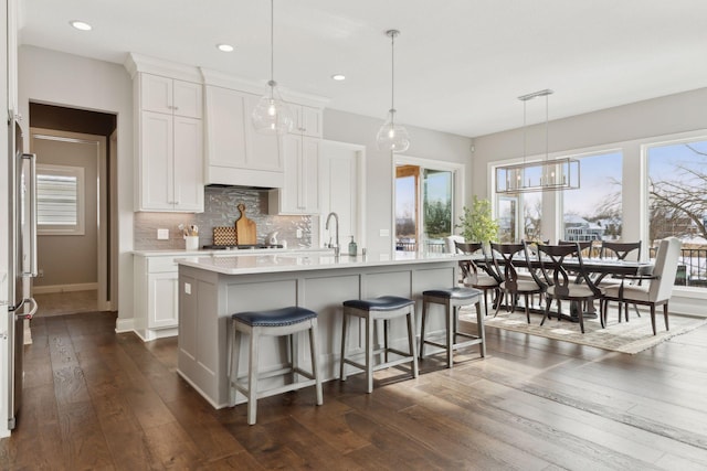 kitchen with white cabinets, a healthy amount of sunlight, hanging light fixtures, dark hardwood / wood-style floors, and a kitchen island with sink