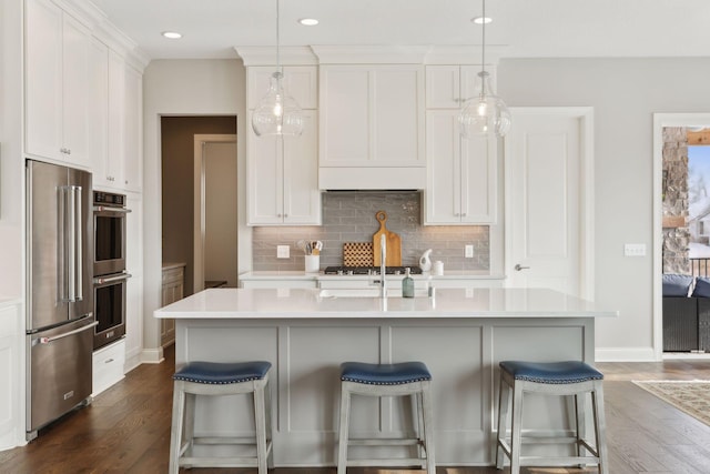 kitchen featuring decorative light fixtures, white cabinets, stainless steel appliances, and a center island with sink