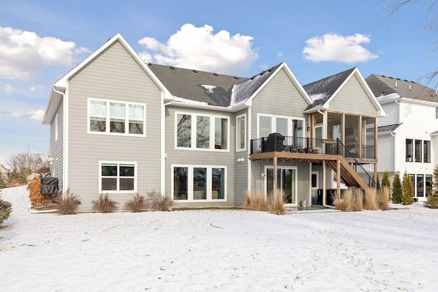 snow covered back of property featuring a deck and a sunroom