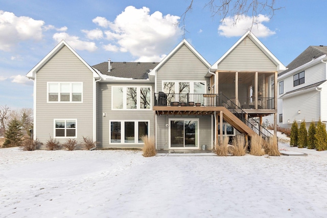 snow covered rear of property with a wooden deck and a sunroom