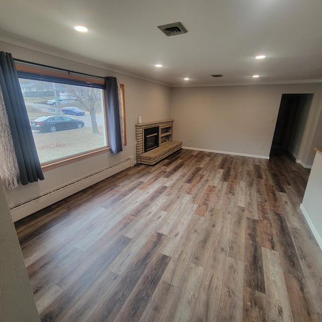 unfurnished living room with hardwood / wood-style flooring, ornamental molding, a baseboard heating unit, and a fireplace