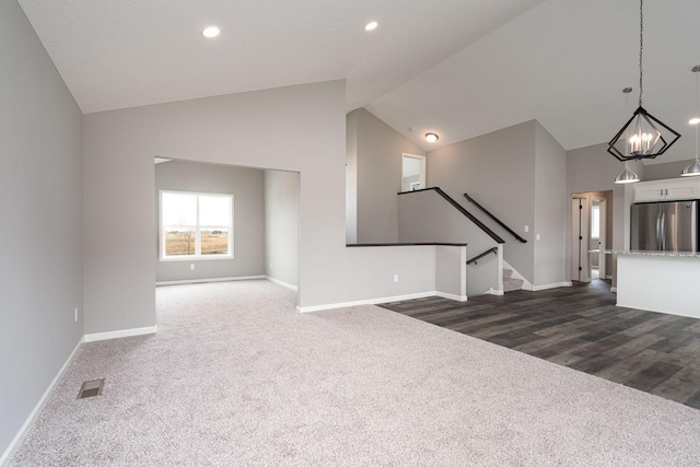 unfurnished living room with high vaulted ceiling, an inviting chandelier, and dark colored carpet