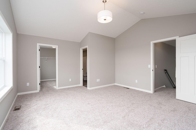 unfurnished bedroom with lofted ceiling, a walk in closet, a closet, and light carpet