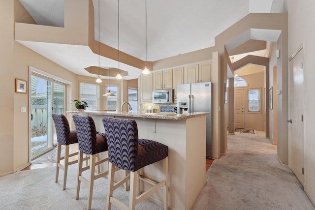 kitchen with stainless steel appliances, light colored carpet, pendant lighting, and light stone countertops