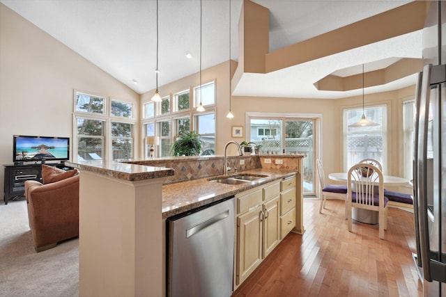 kitchen with stainless steel appliances, sink, hanging light fixtures, light stone countertops, and a center island with sink