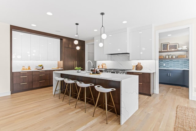 kitchen featuring decorative light fixtures, white cabinetry, light wood-type flooring, a breakfast bar area, and a kitchen island with sink