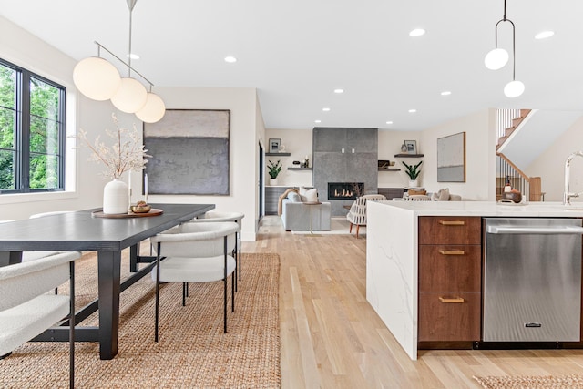 kitchen featuring a fireplace, light wood-type flooring, dishwasher, and pendant lighting