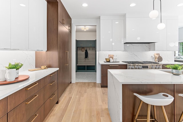 kitchen with pendant lighting, light wood-type flooring, backsplash, white cabinets, and stove