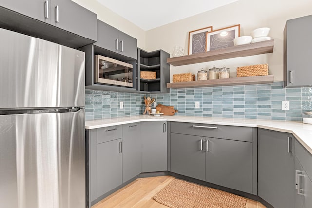 kitchen with decorative backsplash, light wood-type flooring, gray cabinetry, and appliances with stainless steel finishes