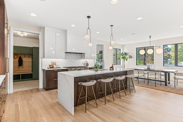 kitchen with white cabinetry, an island with sink, decorative backsplash, sink, and light hardwood / wood-style flooring