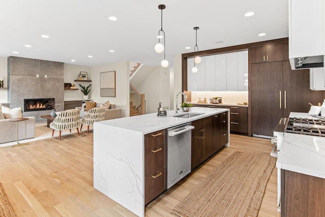 kitchen with white cabinets, dishwasher, a tiled fireplace, sink, and decorative light fixtures