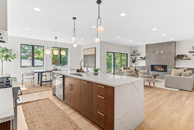 kitchen with appliances with stainless steel finishes, an island with sink, a fireplace, sink, and decorative light fixtures