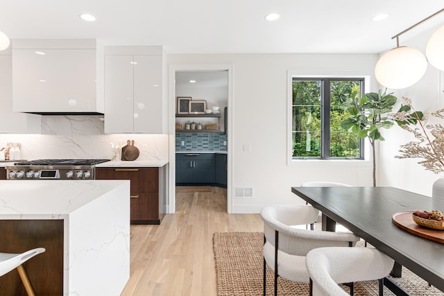 kitchen featuring pendant lighting, light hardwood / wood-style floors, stainless steel gas stovetop, backsplash, and white cabinets