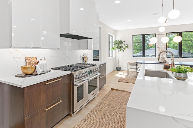 kitchen with range with two ovens, wall chimney exhaust hood, decorative light fixtures, decorative backsplash, and sink