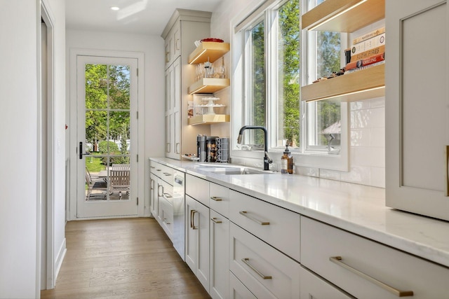 interior space featuring tasteful backsplash, stainless steel dishwasher, sink, light hardwood / wood-style flooring, and light stone counters