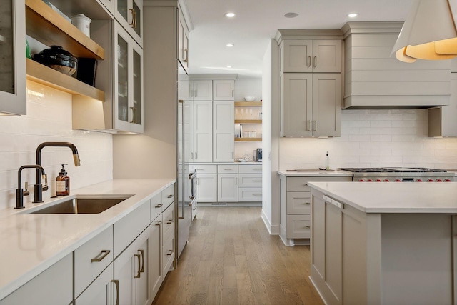 kitchen featuring range, tasteful backsplash, sink, light wood-type flooring, and light stone counters