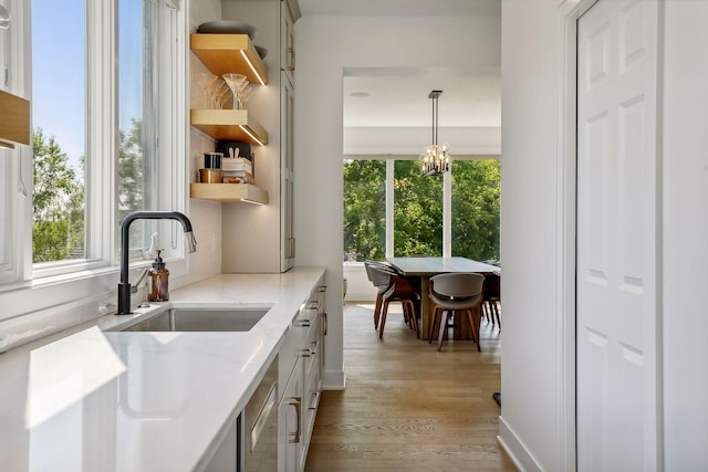 kitchen with pendant lighting, sink, an inviting chandelier, light wood-type flooring, and light stone counters