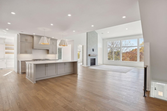 kitchen with decorative light fixtures, tasteful backsplash, light hardwood / wood-style floors, premium range hood, and gray cabinets