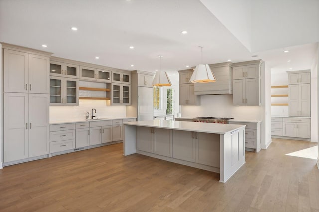 kitchen with a large island, built in refrigerator, light wood-type flooring, pendant lighting, and sink