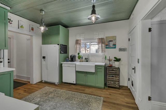 kitchen with white appliances, decorative light fixtures, wood-type flooring, sink, and green cabinetry