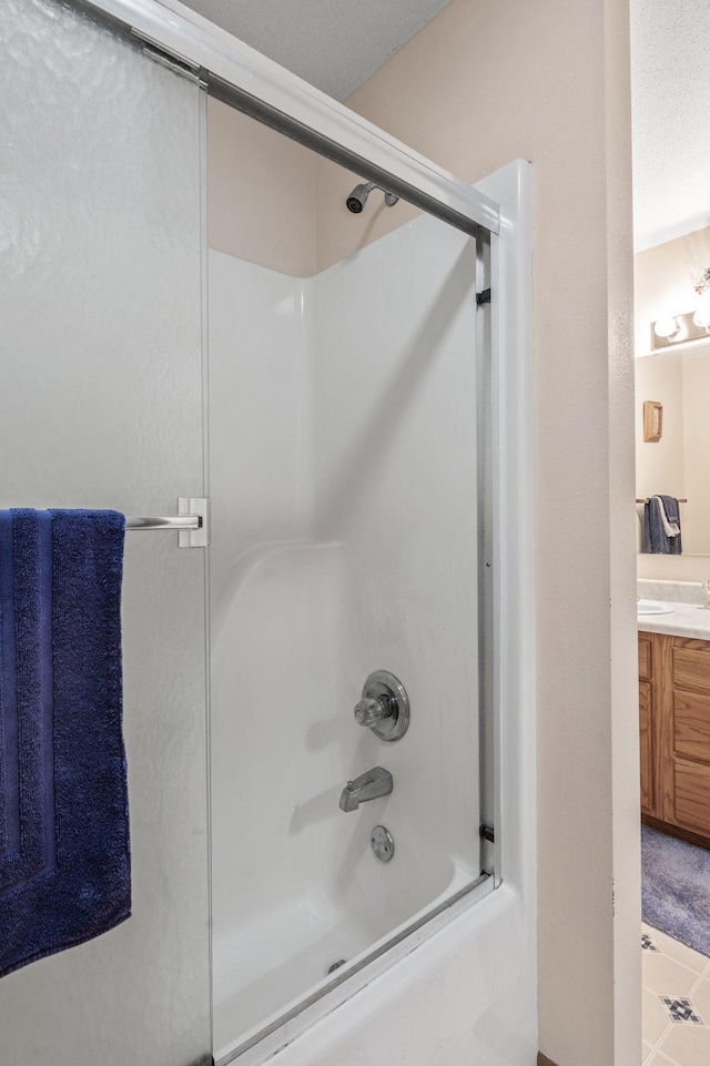 bathroom featuring vanity, combined bath / shower with glass door, and a textured ceiling