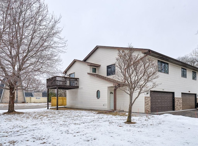 snow covered house with a garage and a wooden deck