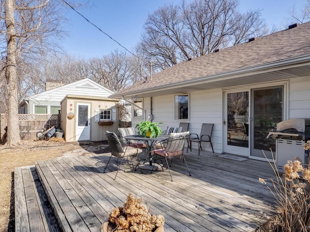 deck with outdoor dining area, an outbuilding, a grill, and fence