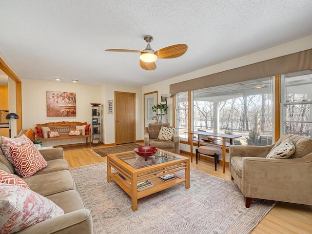 living area with a ceiling fan, baseboards, light wood finished floors, and a textured ceiling