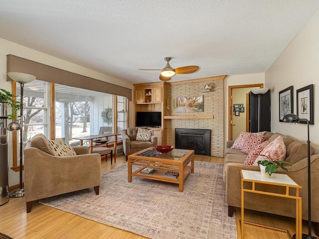 living area featuring a fireplace, light wood-style flooring, a ceiling fan, and a textured ceiling