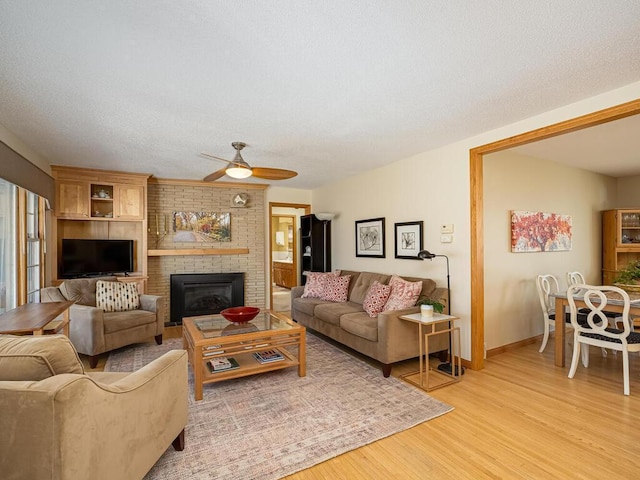 living room with light wood-style flooring, a textured ceiling, ceiling fan, and a fireplace