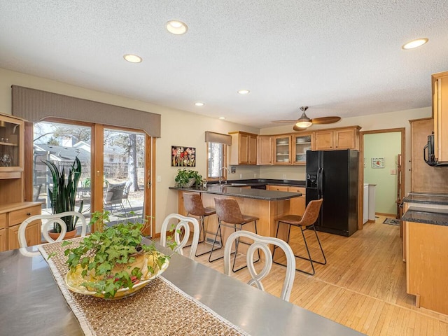 kitchen featuring a peninsula, ceiling fan, black appliances, glass insert cabinets, and a kitchen breakfast bar