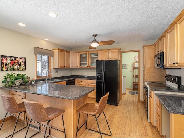 kitchen with light brown cabinets, a breakfast bar area, a peninsula, black appliances, and a sink