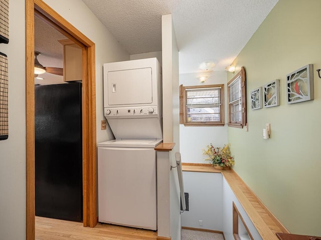 washroom featuring laundry area, light wood-type flooring, stacked washer and clothes dryer, and a textured ceiling