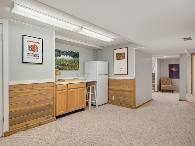 kitchen with wooden walls, visible vents, freestanding refrigerator, wainscoting, and light carpet