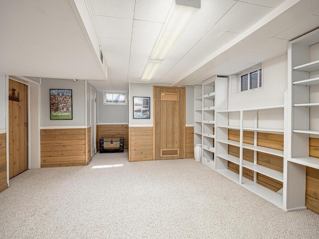 basement featuring a wainscoted wall, visible vents, wood walls, and carpet flooring