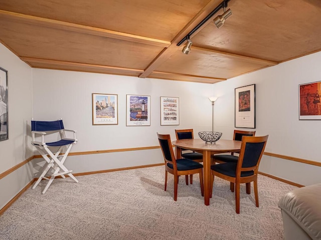 carpeted dining room featuring track lighting, beamed ceiling, and baseboards