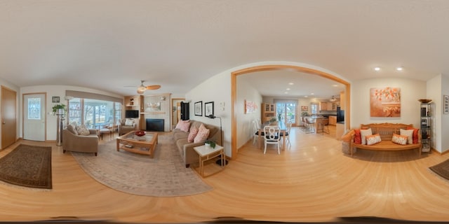 living area with arched walkways, a ceiling fan, wood finished floors, and a fireplace