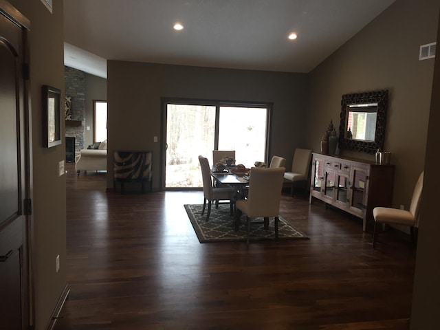 dining area with dark hardwood / wood-style floors, lofted ceiling, and a fireplace