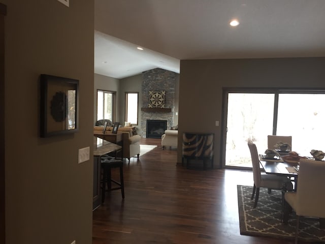 dining area with lofted ceiling, a healthy amount of sunlight, dark hardwood / wood-style flooring, and a stone fireplace