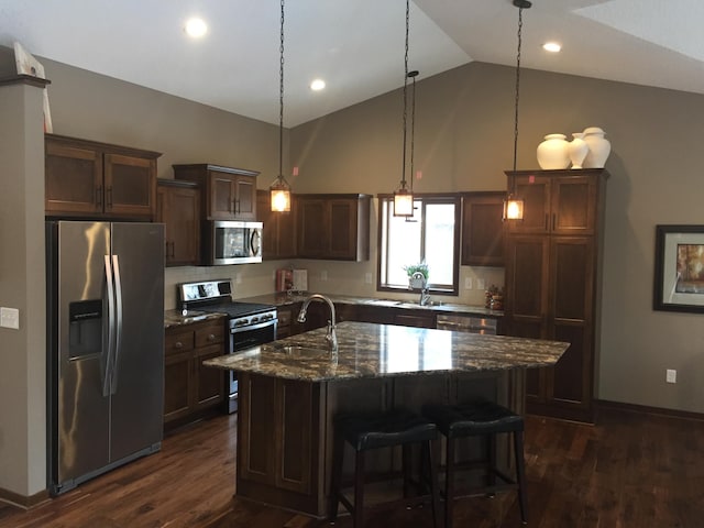 kitchen with dark stone countertops, a center island with sink, sink, hanging light fixtures, and stainless steel appliances