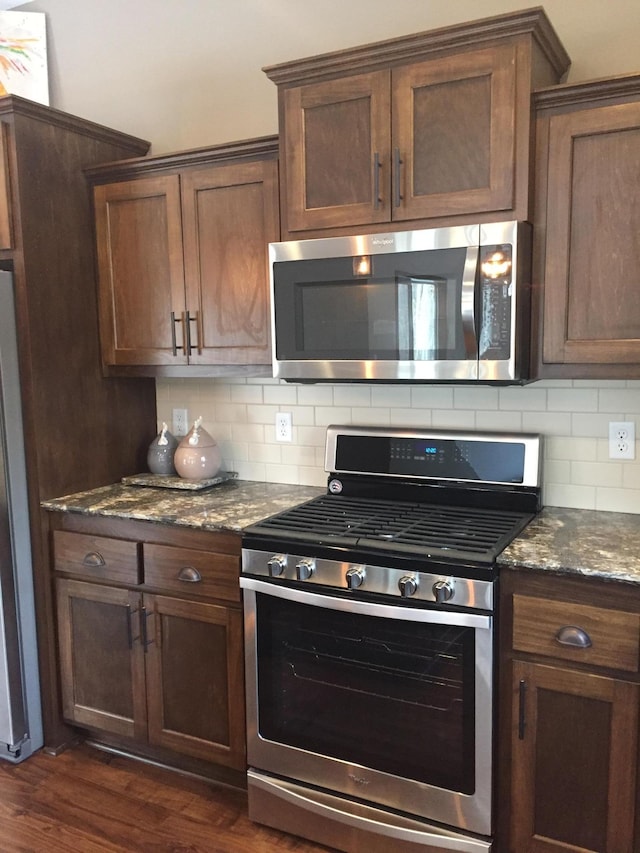 kitchen with appliances with stainless steel finishes, dark hardwood / wood-style flooring, backsplash, and stone countertops