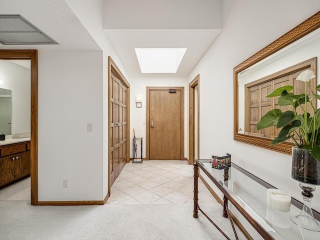 hall with visible vents, baseboards, light carpet, light tile patterned floors, and a skylight